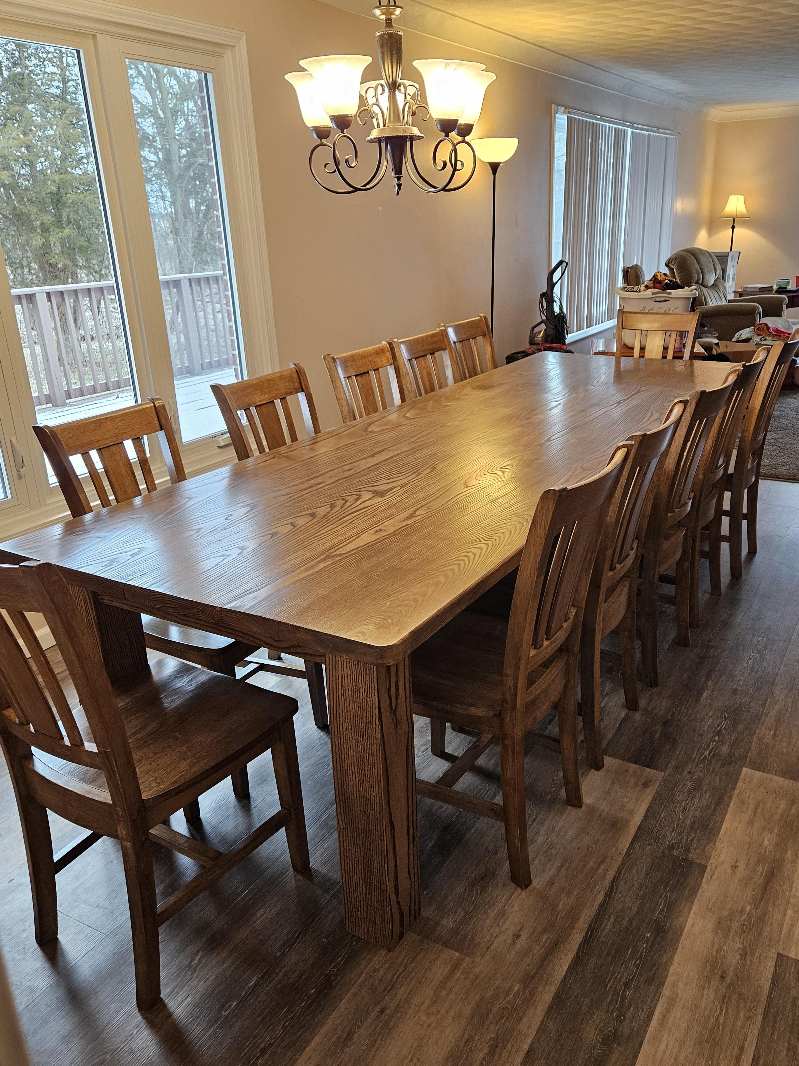 Wooden dining table with chairs in a well-lit room with large windows.